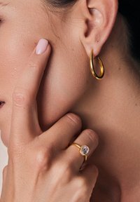 Złoty kolczyk w kształcie obręczy o gładkim, zaokrąglonym kształcie; złoty pierścionek z okrągłym kamieniem otoczonym mniejszymi kamieniami, osadzony w wypolerowanej obrączce.