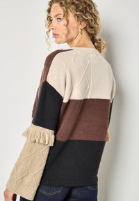 Maglione lavorato a maglia con un design multicolore, caratterizzato da strisce beige, bordeaux, nere e crema; maniche testurizzate con frange e dettagli a trecce.