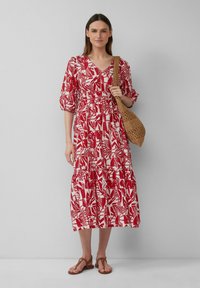 Rode en witte bloemenpatroon maxi-jurk met een V-hals, pofmouwen, een elastische taille en een gelaagde rok. Draagt men met bruine sandalen en een geweven tas.