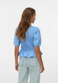 Blusa smocked azzurro chiaro con maniche a palloncino, orlo arricciato e tessuto testurizzato, abbinata a jeans in denim chiaro.