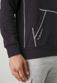 Sudadera morada oscura con detalles de costura blanca y un bolsillo tipo canguro. Puños y dobladillo acanalados, que presenta bordado de "New York Yankees".