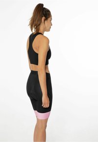 Crni sportski crop top i prilagođene kratke hlače s ružičastom trakom na rubu. Materijal izgleda glatko s teksturiranim završetkom na hlačama.