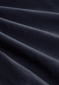 Tissu bleu marine à la texture lisse, présentant des plis doux et un léger éclat. Le matériau semble léger et souple.