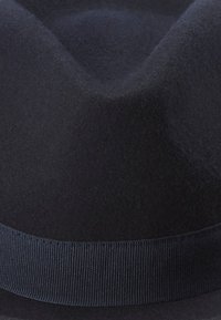 A dark navy felt fedora with a ribbon band sits against a neutral background, showcasing its smooth texture and elegant design.