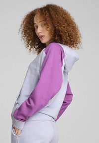 Felpa leggera grigia e viola con una texture morbida, cappuccio e maniche colorate. Dettaglio logo discreto sul davanti.