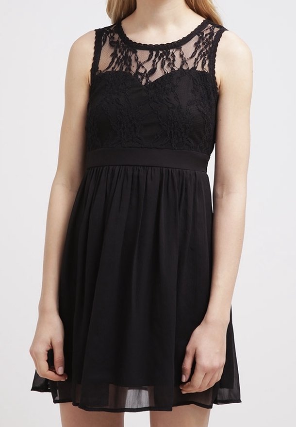 Femme portant une robe noire sans manches avec corsage en dentelle et encolure transparente, taille cintrée et jupe fluide.
