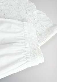 White garment sleeve with elastic cuff and lace detailing featuring floral and heart-shaped cutouts on light background.