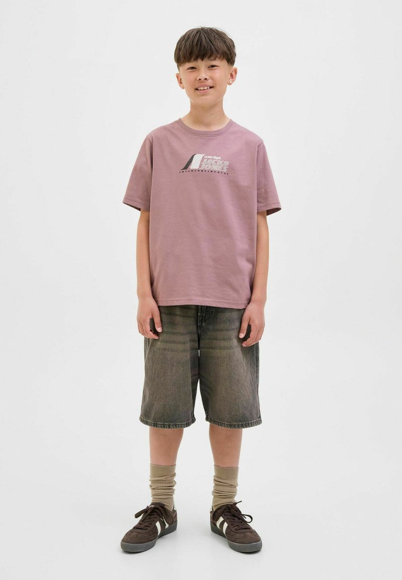 Korte mouwen, pastelroze katoenen t-shirt met grafische print, gecombineerd met denim shorts tot de knie en bruine sneakers. Lichtgekleurde sokken.
