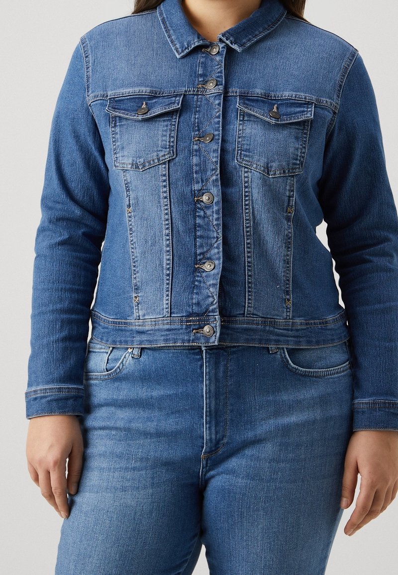 Jeansjacka i mellanblå denim med krage, två bröstfickor och knäppning med knappar. Långa ärmar med manschetter och en figursydd fåll.