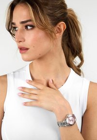 Orologio d'argento con quadrante rosa, cassa rotonda e cinturino in metallo. L'orologio presenta indicatori delle ore luminosi e una corona per la regolazione dell'ora.