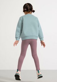 Lyseblå sweatshirt med ribbede manchetter, parret med tætsiddende, lyserøde tights. Fodtøjet har et flerfarvet design med en solid sål.