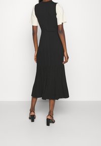 Abito midi nero a coste, con maniche corte color crema; presenta dettagli perforati all'orlo ed è abbinato a sandali con tacco quadrato.