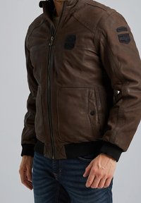 Giacca bomber in pelle marrone con chiusura a zip, polsini a coste neri e toppe sulle spalle. Presenta tasche laterali e una finitura testurizzata.