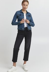 Jeans jakna v srednjem pranju z gumbom spredaj, dvema žepoma na prsih in kontrastnim šivom. V kombinaciji z črnimi hlačami z visokim pasom in belimi supergami.