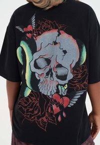 Sort oversized t-shirt med et flerfarvet kraniegrafik, roser, et hjerte og vinger. Tekstureret print med livlige farver på ryggen.