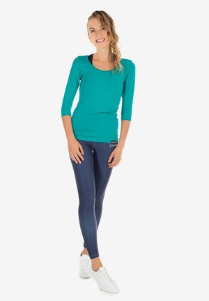 Teal fitted top with three-quarter sleeves, paired with navy leggings and white sneakers. Smooth texture, simple design, and no visible patterns.