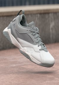 Sneaker alb și gri deschis cu panouri din plasă, design rotund, șireturi plate și talpă texturată. Prezintă un logo și un guler căptușit.