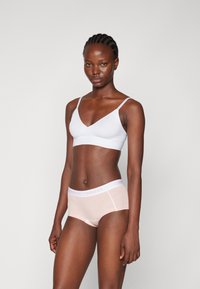 Lys blå bralette med tynne stropper, parret med nude hipster truser som har en hvit midjebånd med 'PIECES'-logo i lys rosa.
