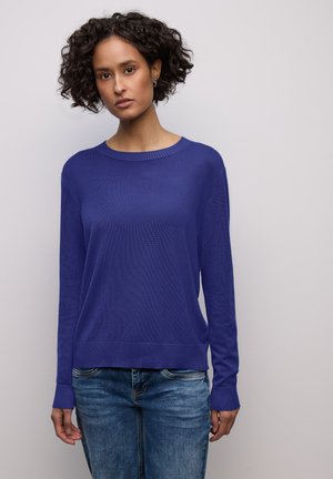 Pull violet en maille avec manches longues, col et poignets côtelés. Assorti à un jean en denim bleu clair pour un look décontracté.