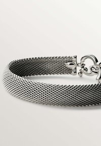 Pulsera de malla plateada con un diseño flexible y trenzado. Cuenta con un brillante cierre de langosta y acentos redondos. Textura suave con un acabado metálico.
