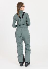 Skidräkt i dämpad grön med tygband och elastisk midja. Justerbara ärmslut med svarta detaljer och förstärkta bootområden.