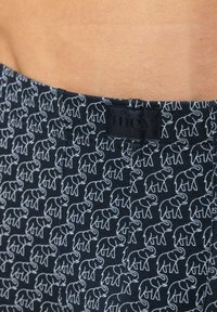 Tissu noir avec motif d'éléphants blancs, présentant une texture lisse et une ceinture étiquetée "mey." Le design met en avant un motif animalier ludique.