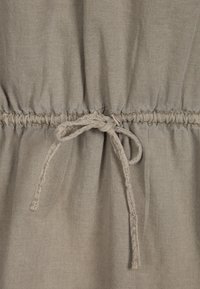 Tessuto grigio chiaro con vita arricciata, dotato di un laccio di chiusura realizzato con materiale abbinato. Texture liscia con dettagli di cucitura sottili.