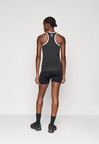 Top atlético preto com detalhes brancos e um logo nas costas, combinado com calções pretos e sapatos pretos. Linhas limpas e设计 ajustado.
