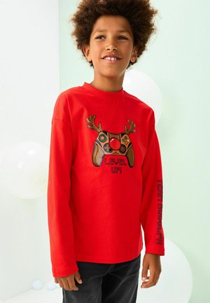 Kind mit lockigem Haar, das ein rotes Langarmshirt mit einem Gaming-Controller mit Rentiergeweih und dem Text "LEVEL UP!" trägt