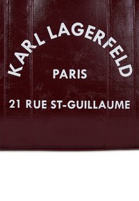 Burgundy, glossy tote bag with embossed text: "KARL LAGERFELD PARIS" and "21 RUE ST-GUILLAUME" in white. Soft, textured material, no visible hardware.