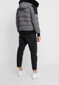 Grå puffjacka med svart axelpanel och huva i konstpäls, kombinerad med mörka jeans och vita sneakers för en avslappnad look.