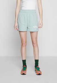 Person wearing light blue Nike shorts, white top, dark green socks, and orange and green sneakers standing against a plain background.