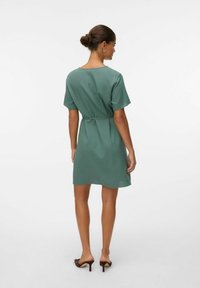 Abito a maniche corte, lungo fino al ginocchio, in tessuto verde tenue; presenta una vita stretta con un design semplice e una scollatura posteriore.