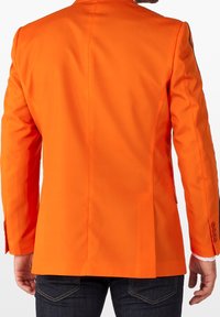 Pomarańczowa marynarka szyta na miarę o gładkiej teksturze, z jednym rozcięciem z tyłu i trzema guzikami na rękawach, połączona z ciemnymi dżinsami.
