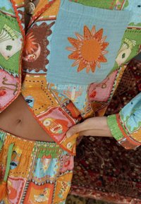 Gepersonaliseerde katoen loungewear set met levendige kleuren zoals oranje en blauw, afgewerkt met bloemen- en gezichtenmotieven, evenals contrasterende stiksels.