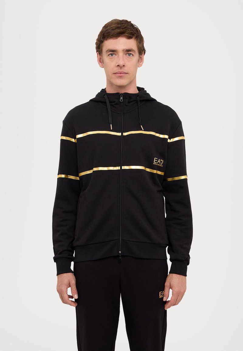 Black zip-up hoodie with gold striped accents and logo. Made of soft material, features a hood and drawstrings, ribbed cuffs and hem.