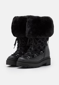 Bottes d'hiver noires avec larges manchettes en fausse fourrure, lacets sur le devant, tissu à motifs et semelles en caoutchouc épaisses.