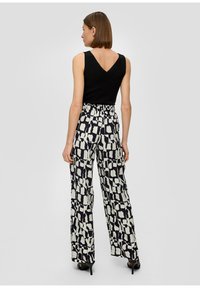 Top sans manches noir avec un décolleté en V, associé à un pantalon à jambe large dans un motif abstrait noir et blanc. Tissu lisse avec une taille élastique.
