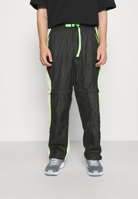 Svarta träningsbyxor med mesh-sidopaneler i neongrönt, elastisk midja, justerbar dragsko och kontrasterande detaljer.