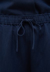 Granatowe lniane spodnie mają elastyczny pasek w talii z wiązaniem z przodu, prezentując gładką teksturę i prosty design.