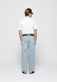 Camiseta blanca, jeans de pierna ancha de color azul claro, cinturón negro con herrajes plateados y sandalias negras con suela blanca. Fondo neutro.