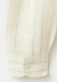 Manche de chemise en coton blanc avec de fines rayures verticales noires, poignet boutonné, et deux boutons couleur crème sur le plastron et le poignet.