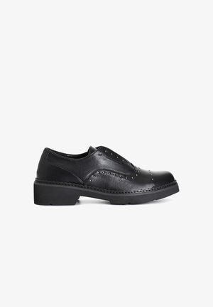 Scarpa nera in pelle con punta arrotondata, design slip-on, decorazioni a borchie lungo la parte superiore e suola in gomma spessa con dettagli intrecciati.