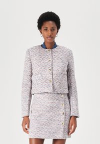 Veste en tweed tissée rose, bleue et blanche avec un col rond et des boutons dorés. Associée à une jupe assortie avec des boutons sur les côtés.