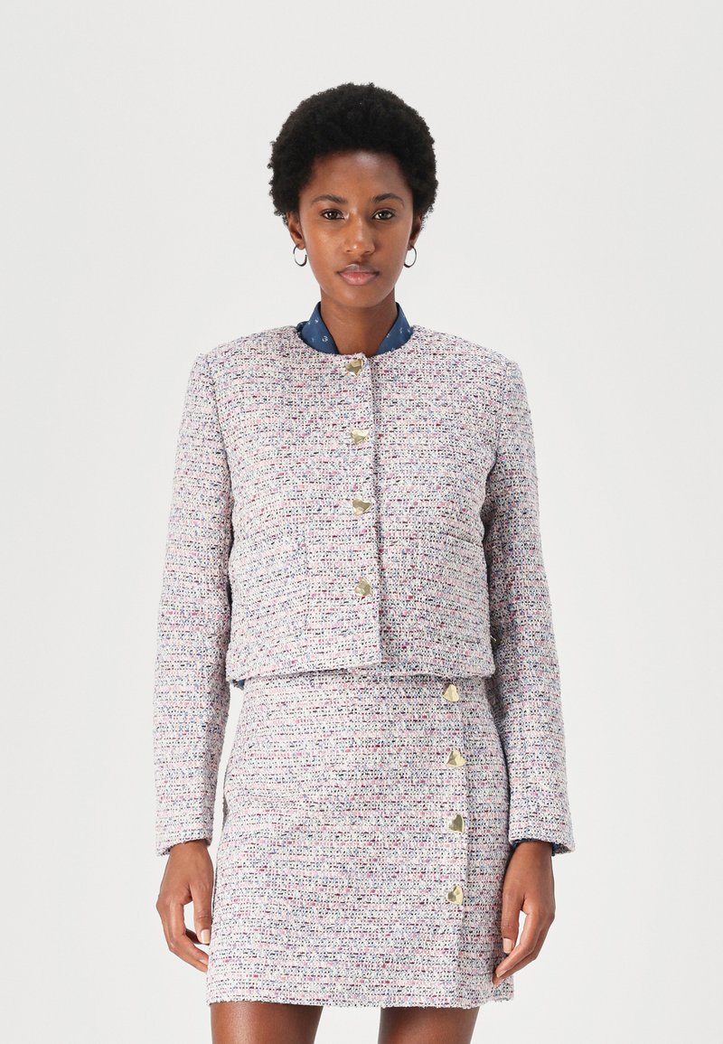 Veste en tweed tissée rose, bleue et blanche avec un col rond et des boutons dorés. Associée à une jupe assortie avec des boutons sur les côtés.