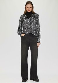 Blouse imprimé serpent noir et blanc à manches longues, décolleté en V, associée à un jean noir taille haute et des bottes noires épaisses. Fini textile lisse.