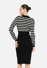 Robe pull rayée noir et blanc avec manches longues, design ajusté, poignets côtelés et transition sans couture vers une jupe noire unie.
