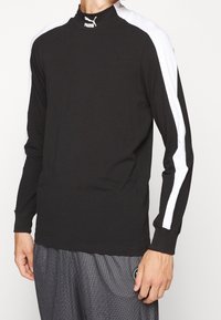 Czarna koszula z długim rękawem z białymi paskami na ramionach, miękka tkanina, dopasowany krój oraz logo Puma na kołnierzyku. Strój codzienny.