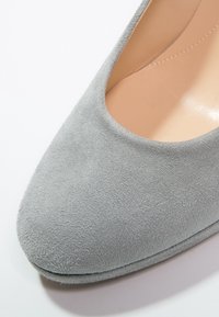 Chaussure à talon haut en suede gris avec un bout arrondi et un intérieur lisse. Présente une silhouette épurée et une texture subtile sur le matériau supérieur.