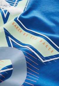 Niebieska i miętowa tkanina w wzory geometryczne, z pomarańczowym napisem "BAKER BY TED BAKER" na gładkiej, lekko teksturowanej powierzchni.